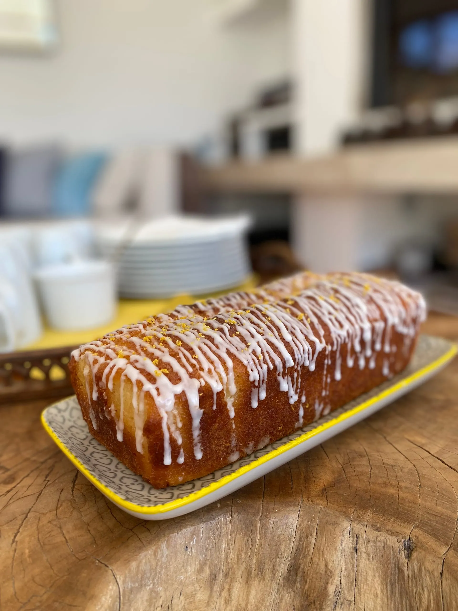 A lemon drizzle loaf, iced and scattered with zest, waiting on a plate in the chalet