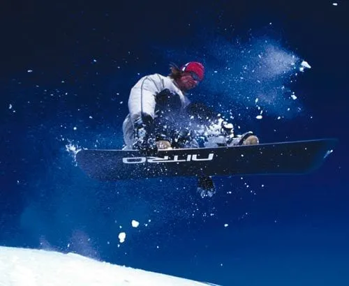 Lloyd mid-air on a snowboard against a deep blue sky, snow flying from the board